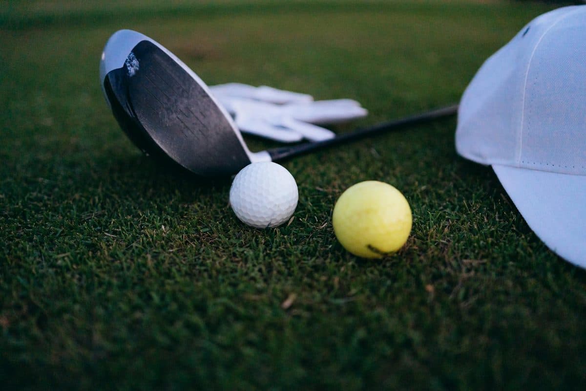 Golf club, golf balls and a cap laid out on grass