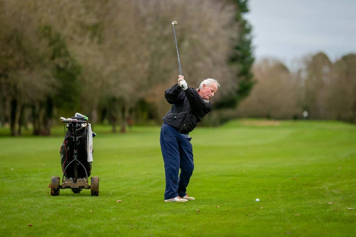 Elderly man swinging a golf club on a vibrant golf course