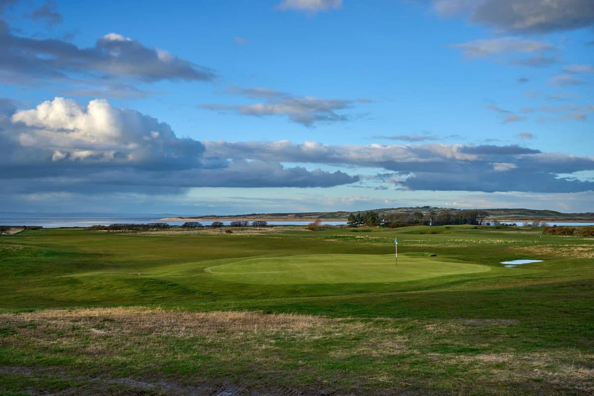 A picturesque Scottish golf course with lush green fairways under a clear blue sky